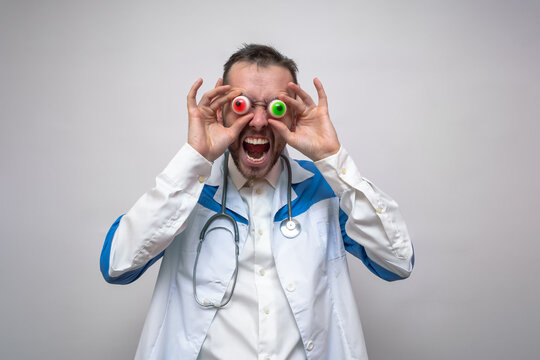 Evil doctor holds colored eyeballs near his face. Concept of a creepy doctor