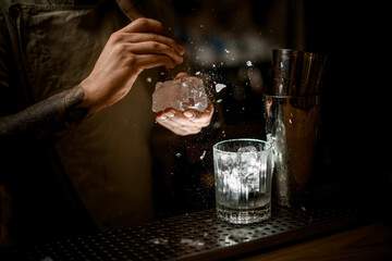 bartender holds ice and breaks off pieces from it and glasses stands nearby