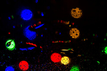 Colorful bokeh lights on a dark background behind the raindrops on the glass texture 