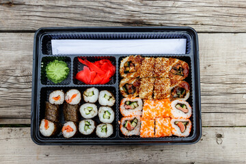 Set of sushi rolls in plastic box on wooden table. Sushi for take away or delivery of sushi in plastic container. Top view