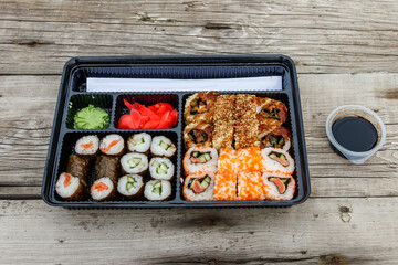 Set of sushi rolls in plastic box on wooden table. Sushi for take away or delivery of sushi in plastic container