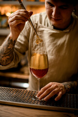 bartender holds golden piece of ice over glass decorated with gold and look at it