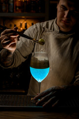 bartender at bar holds golden piece of ice over steaming wine glass and look at it