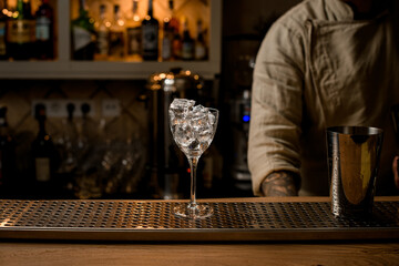 wine glass with ice cubes and shaker cup stands on the bar.