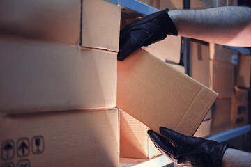 Hands of a man in leather gloves take a box of goods in a warehouse at night. Concept of security...