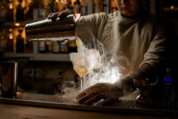 view of barman pouring steaming drink from shaker cup into wine glass