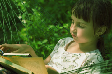 Young beauutifuul girl enjoying a book reading in comfortable hammock outdoors at green garden
