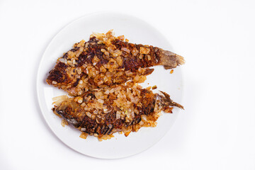 Fried crucian fish in breadcrumbs and onions in a plate on a white background. Golden crust of breadcrumbs. Freshwater fish.