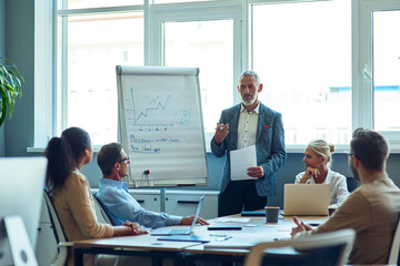 Confident mature businessman giving a presentation, explaining something to colleagues while having a meeting in the office