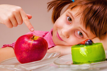 Close up portrait of beauiful young girl looking a red apple and green cake. She prefer fruits than sweets spot. Health, diet, lifestyle concept.