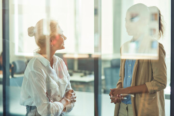 Obraz premium Two diverse female coworkers having informal conversation while standing in the modern office
