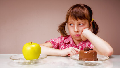 Dieting and healthy food concept. Very hard choice between fruits and sweets. Portrait of young beautiful girl choosing between apple  and tasty cake.  Horizontal image.