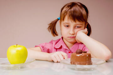 Dieting and healthy food concept. Very hard choice between fruits and sweets. Portrait of sad young beautiful girl choosing between apple  and tasty cake.