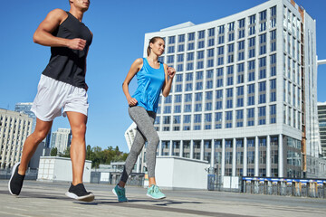 Young man and woman running along city street