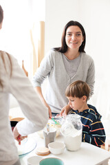 Mom in white clothes with her son bake a pie from white flour on a white background