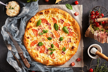 Capricciosa pizza with cheese, bacon and tomatoes and basil, on a dark background, top view