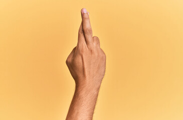Arm and hand of caucasian man over yellow isolated background gesturing fingers crossed, superstition and lucky gesture, lucky and hope expression