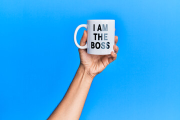 Hand of hispanic man holding i am the boss coffee cup over isolated blue background.