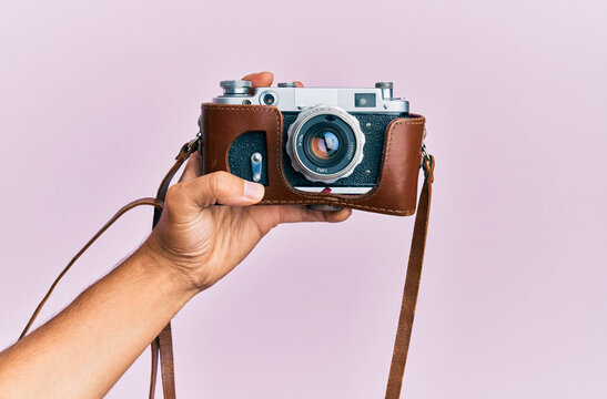 Hand of young hispanic man holding vintage camera over isolated pink background.