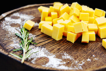 Cheese cubes on a wooden tray decorated with a sprig of greens. Ingredient for preparing meals from dairy products. Close-up