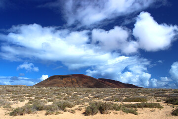 Panoramic view of Agujas Grandes volcano under a blue sky streaked with white clouds. La Graciosa, Lanzarote, Canary Islands, Spain.