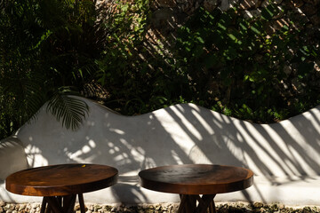 Empty wooden tables in front of tropical green floral background with palm tree leaf shadows