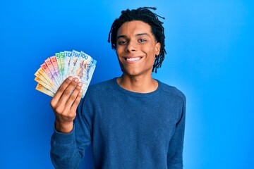 Young african american man holding swiss franc banknotes looking positive and happy standing and smiling with a confident smile showing teeth