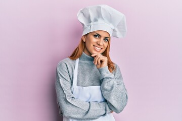 Hispanic young woman wearing professional cook uniform and hat smiling looking confident at the camera with crossed arms and hand on chin. thinking positive.