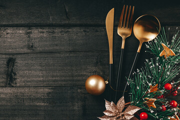 Golden cutlery and christmas ball on black wooden background, concept of new year table setting in...