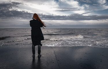 Lonley woman from behind standing at the beach on a stormy day with cloudy sky