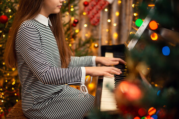 Playing the piano at christmas time at home. Shot of a girl`s hands on pino keyboard with festive...