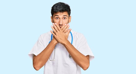 Young handsome man wearing doctor uniform and stethoscope shocked covering mouth with hands for...