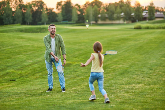 Happy father playing badminton with his joyful little daughter outdoors in the park on a summer day