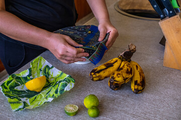 Close up of woman wrapping fruits in environmentally safe beeswax wrap. Reusable eco-friendly kitchen products. Zero waste sustainable plastic free lifestyle