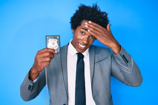 Handsome african american man with afro hair holding detective badge stressed and frustrated with hand on head, surprised and angry face
