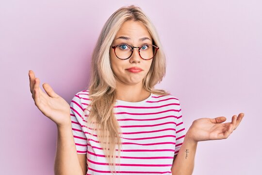 Beautiful caucasian blonde girl wearing casual clothes and glasses clueless and confused with open arms, no idea and doubtful face.