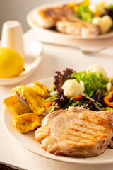 Fried pork entrecote on the bone with stewed pumpkin pieces and salad in a plate close up, green salad with cauliflower and napa cabbage, bell pepper and spices