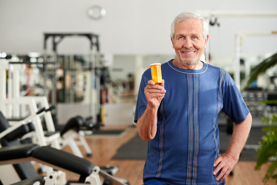 Senior man holding bottle of pills at gym. Portrait of elderly caucasian man showing pills. Best vitamins for men.