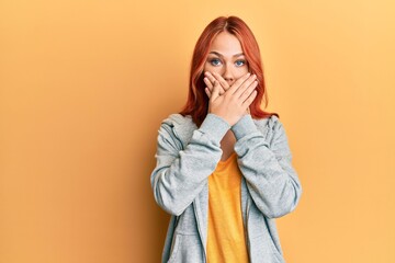 Young beautiful redhead woman wearing casual sporty sweatshirt shocked covering mouth with hands for mistake. secret concept.