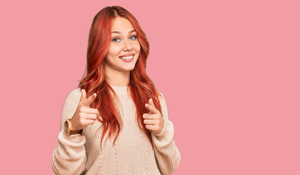 Young redhead woman wearing casual winter sweater pointing fingers to camera with happy and funny face. good energy and vibes.