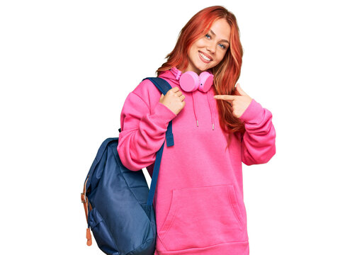 Young redhead woman holding student backpack and books pointing finger to one self smiling happy and proud