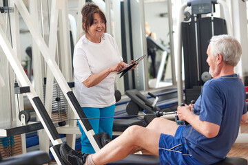 Senior woman at gym using digital tablet. Elderly man working out at fitness center. Training according plan. People, sport and technology concept.
