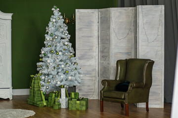 Stylish white Christmas tree in the interior, next to a green chair and a lot of gift boxes. Space for text