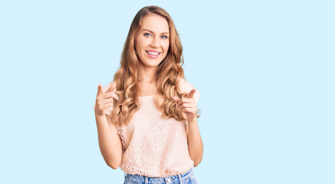 Young beautiful caucasian woman with blond hair wearing casual clothes pointing fingers to camera with happy and funny face. good energy and vibes.
