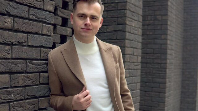 Portrait of a stylish businessman in brown coat on brick wall background
