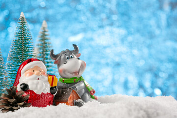 Christmas decoration with natural blurred background. Santa Claus and the 2021 symbol bull stand in the snow