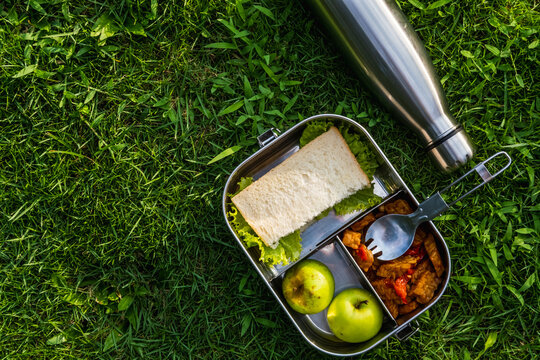 Stainless steel container or lunch box with healthy vegetarian meal and reusable thermo bottle on grass background. Eco-friendly kitchen products. Zero waste sustainable plastic free lifestyle