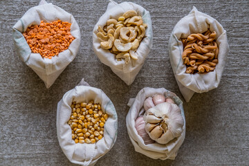 Variety of different groceries in cotton bags packed for storage: pasta, nuts, grains on stone background. Eco-friendly organic bio kitchen products. Zero waste sustainable plastic free lifestyle