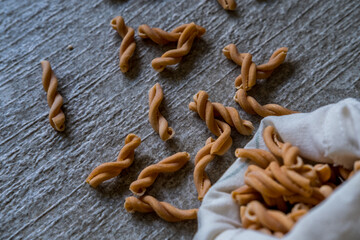 Short pasta in cotton textile bag spilled on stone grey background. Eco-friendly organic bio kitchen products. Zero waste sustainable plastic free lifestyle