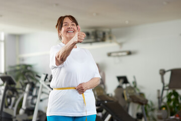 Senior woman measuring her waist at gym. Mature woman expressing success after measuring herself...